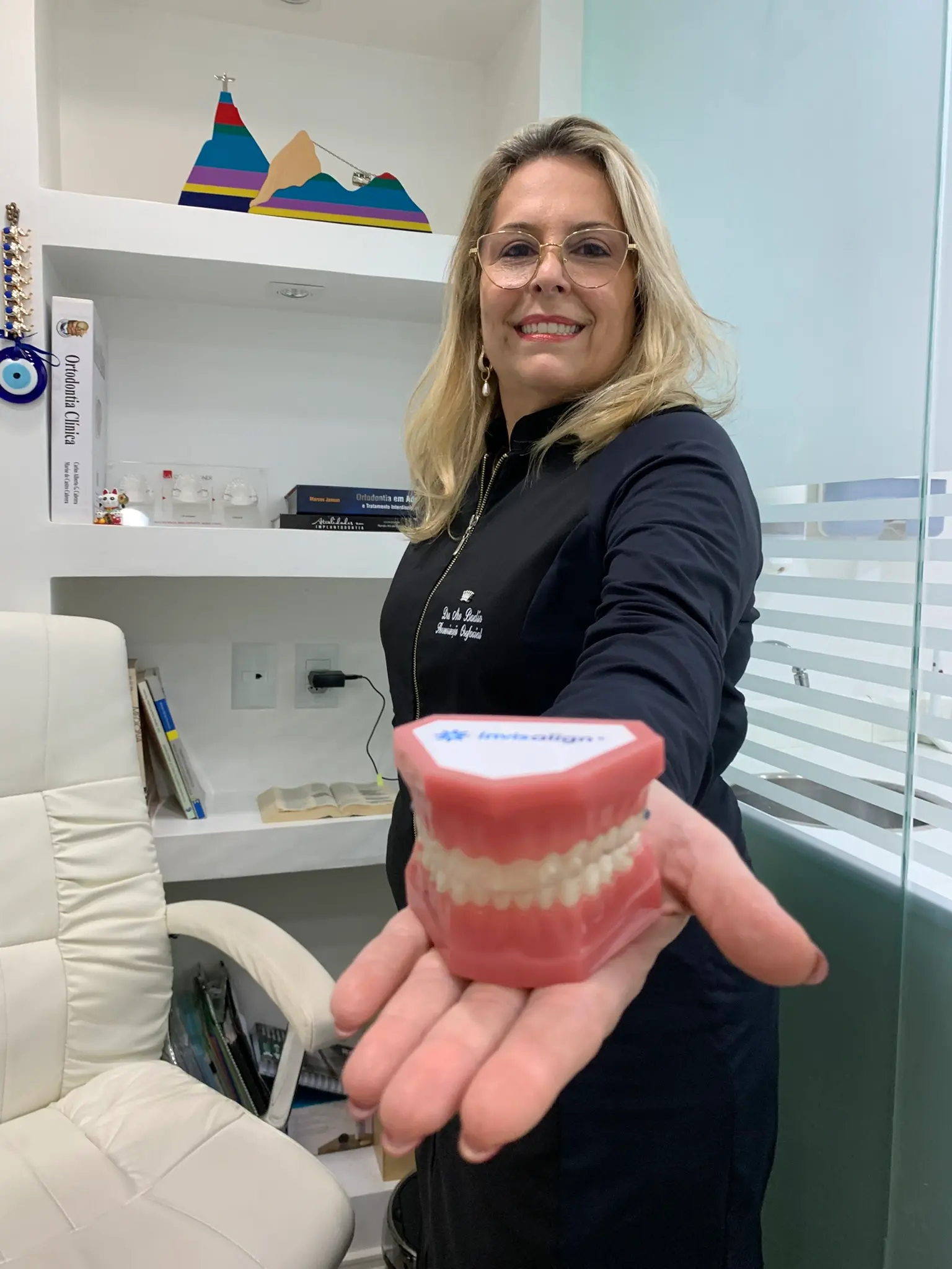 Dra. Ana Badin segurando arcada com alinhador Invisalign no consultório